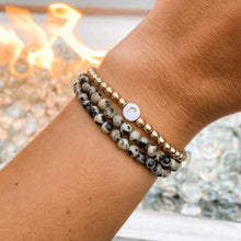 Load image into Gallery viewer, Dalmation Jasper bracelet pictured on a wrist with a gold bracelet.
